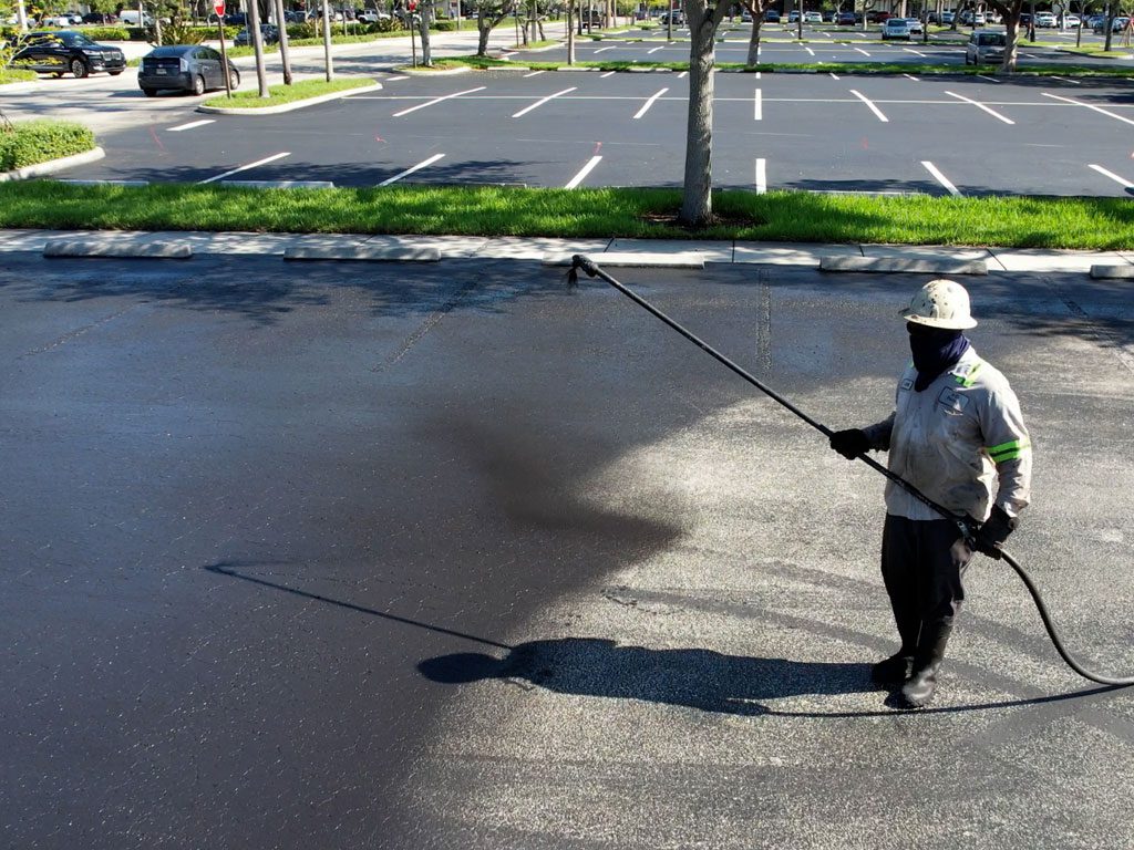 Sealcoating company near me in Fort Lauderdale, 3-D Paving applies sealcoating with an industrial sprayer to a parking lot.