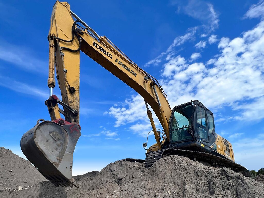 Massive Excavator on the top of a dirt hill at a site development project in Pompano Beach, FL in 2022. Work being done in preparation for a concrete building pad as a foundation to a new retail shopping center.