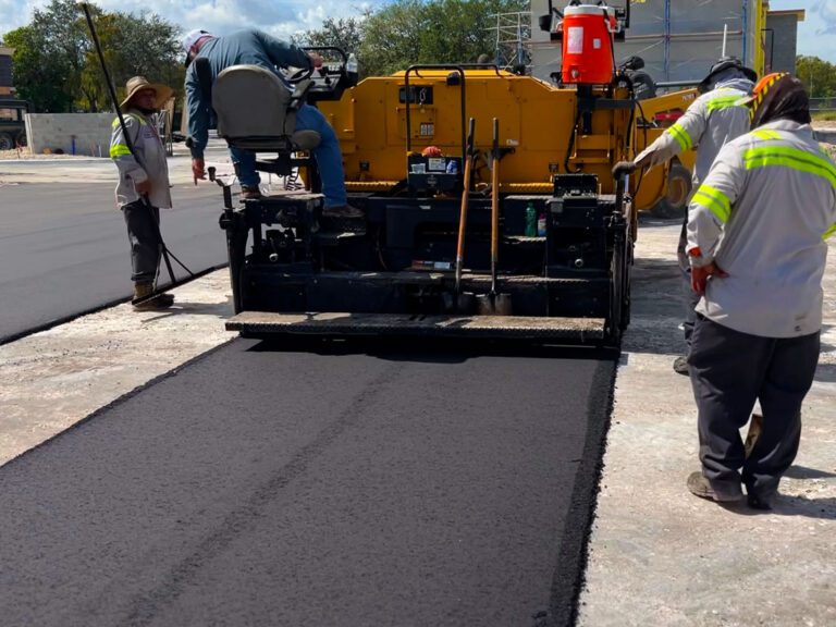 Asphalt paving crew laying a bottom lift of asphalt with an asphalt paving machine at a parking lot installation in Palm Beach County in April of 2023. 3-D Paving and Sealcoating is South Florida's commercial asphalt and concrete paving experts.
