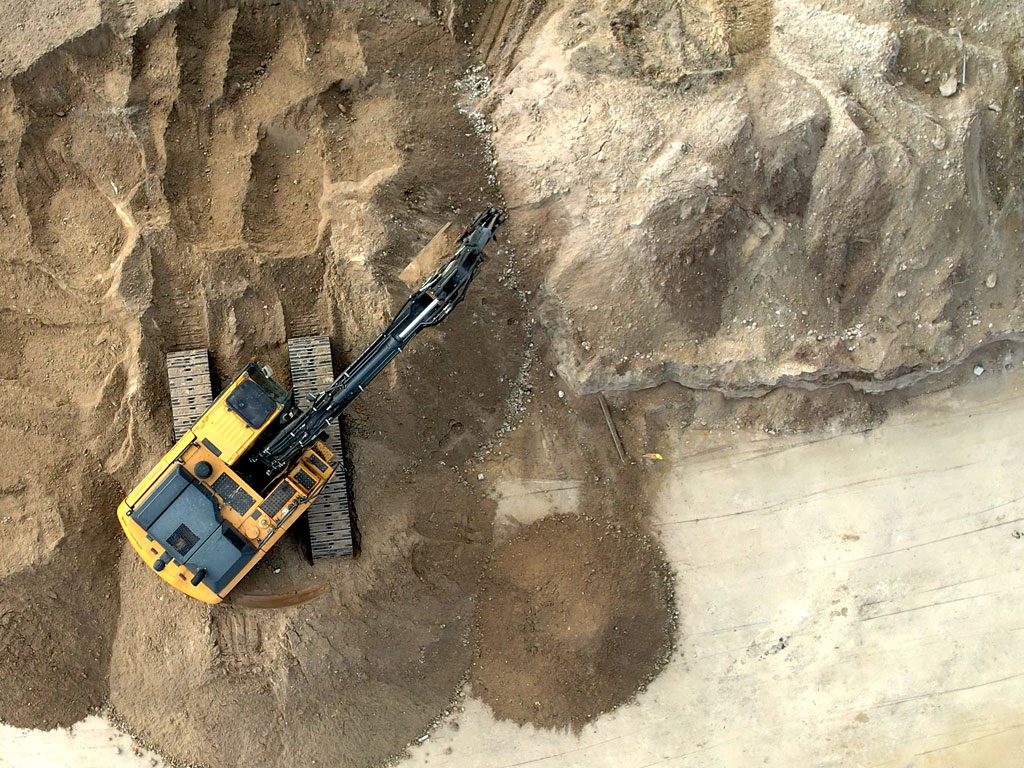 Top down aerial view of a large john deere excavator moving dirt at a large site development in Deerfield Beach, FL in April of 2023 by 3-D Paving and Sealcoating.