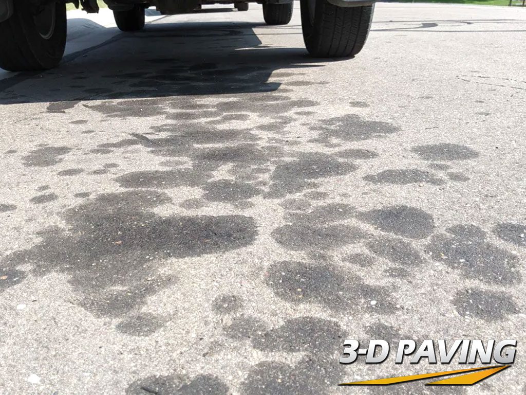 Image taken from a low angle at ground level illustrating oil and grease spots caused by automobiles leaking fluids and oils on asphalt.