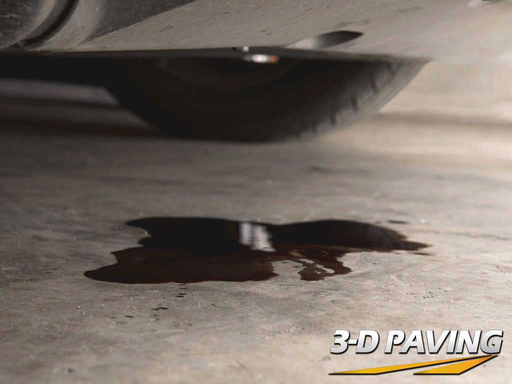 Image taken at a low angle almost ground level showing a fresh puddle of oil onto an asphalt driveway.