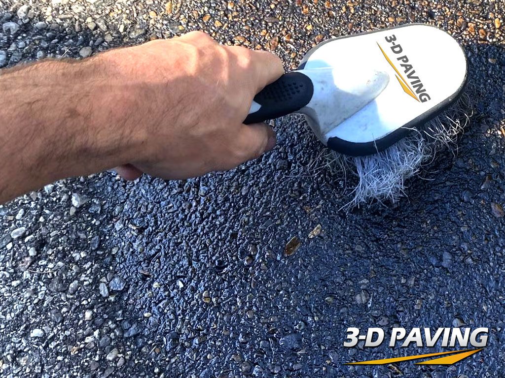 Image taken from above illustrating the removal of oil stains from asphalt by scrubbing and using a scrub brush in conjunction with cleaners to lift oil and grease spots embedded in your asphalt pavements. 